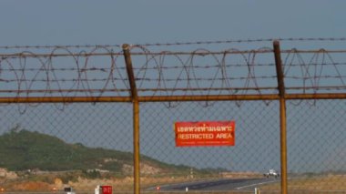 Havalimanı çitleri ve kırmızı yasak bölge tabelası. Tanımlanamayan bir üniforması olan jet uçağı kalkıyor ve tırmanıyor.