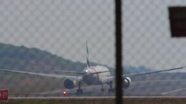 PHUKET, THAILAND - 27 HAZİRAN 2023: Phuket havaalanından kalkmadan önce Emirates 'in 777' lik geniş gövdeli uçağı Boeing 777. Havaalanı çitlerinin arkasında.