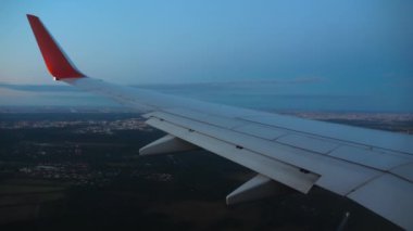 Gün batımında ya da şafakta şehrin üzerinde uçmak. Uçak kanadı, lomboz. Uçak iniyor, pencereden ilk kişi görünüyor.