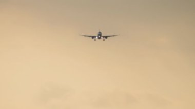 Jet uçağı inişe geçiyor. Yolcu uçağı gün batımında gökyüzünde uçuyor, ön görüş, uzak çekim