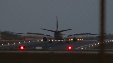 Gün batımında uçak silueti fren yapıyor. Aydınlatılmış pistte bir jet uçağının sinematik çekimi. Turizm ve seyahat kavramı