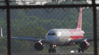 PHUKET, THAILAND - 10 Şubat 2023: Airplane Airbus A320, Tayland Vietnam Jet Air 'in HS-VKP' si inişten sonra fren yapıyor. Uçak geliyor. Havaalanı çitlerinden geçen pistin görüntüsü. Spoiler hazır.