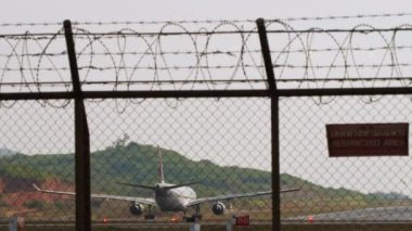 PHUKET, THAILAND - 26 HAZİRAN 2023: Airbus A330, Katar Havayolları A7-AEO Phuket havaalanı kalkış için hızlanır. Havaalanı çitlerinin arkasında, dikiz aynasından, orta mesafeden.