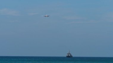 Mavi denizde yüzen kargo gemisi. Arka planda gökyüzünde yüksek bir uçak var. Uçak inişe geçiyor.