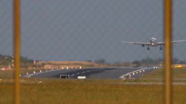 Tanımlanamayan bir üniforması olan, iniş, dokunma ve frenleme yapan bir uçağın yavaş çekim görüntüleri. Havaalanı çitlerinden geçen pistin görüntüsü. İniş ışıklarıyla aydınlatılmış iniş pisti