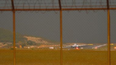 Tanımlanamayan bir üniforması olan uçak havalanmadan önce havalimanı çitinden bakıyor. Uçak kalkıyor. Jet pistte, alacakaranlıkta. Parlak pist