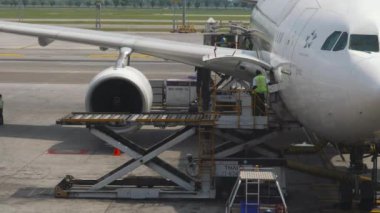 BANGKOK, THAILAND - 14 Kasım 2018: Bangkok havaalanındaki terminal penceresinden bir Tayland Hava Yolları uçağının bakımı. Uçuş yemeklerinin teslimatı. Bagaj ve yiyecek konteynırları boşaltılıyor.
