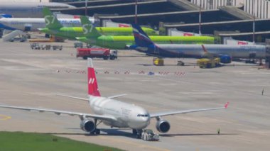 SOCHI, RUSSIA - 27 AĞUSTOS 2022: Airbus A330, RA-73328 Nordwind Havayolları çekici. Traktör ve uçak takside. Terminaldeki diğer uçaklar, Aerobridge 'e yanaştılar.