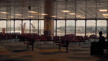 CHANGI, SINGAPORE - 30 HAZİRAN 2025: Bavulları taşıyan uçuş görevlisi Changi Havaalanı terminalindeki boş bir bekleme alanından geçiyor. Hava ekibi işe gidiyor.