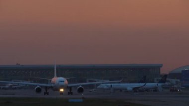 ALMATY, KAZAKHSTAN - 27 Temmuz 2024: Arka planda Air Astana uçaklarının günbatımında, terminalinde ve küresinde taksicilik yapan yolcular