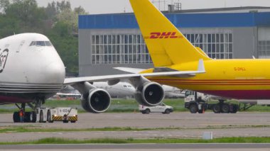 ALMATY, KAZAKHSTAN - 11 Mayıs 2024: Traktör Almaty havaalanında SF Havayolları 'ndan kargo jumbo jeti çekiyor. Havaalanında DHL kargo uçağı var.