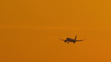 Tanınmayan bir üniformayla altın bir günbatımına inen bir jet görüntüsü..