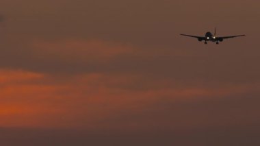 Silüet jet uçağının altın gün batımı bulutlu gökyüzüne inişi görüntüleri yaklaşıyor.