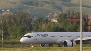ALMATY, KAZAKHSTAN - 24 Haziran 2024: Airbus A321, Air Astana 'dan EI-KGA Almaty havaalanına indikten sonra fren yapıyor. Uçak ve dağ arka planı. Uçak geliyor.