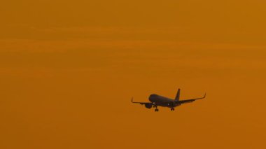 Günbatımında gökyüzünde uçan ticari bir uçak, seyahati ve birinci sınıf hava trafiğini simgeliyor..