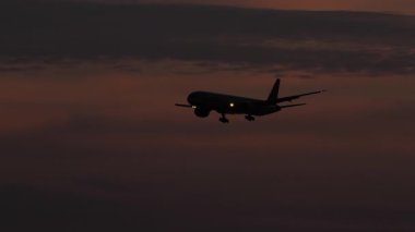 Bir jet uçağının silueti dramatik bir kırmızı günbatımı gökyüzüne doğru uçuyor, akşam alacakaranlığı yaklaşırken. Seyahat, havacılık ve günbatımı temalı projeler için mükemmel..