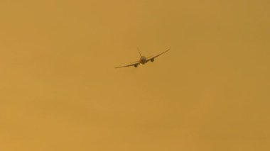 Bir jet uçağının altın bir günbatımı gökyüzünde irtifa kazanmasının çarpıcı sinematik görüntüleri.