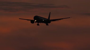 Bir jet uçağının silueti dramatik bir kırmızı günbatımı gökyüzüne doğru uçuyor, akşam alacakaranlığı yaklaşırken. Seyahat ve havacılık için mükemmel..