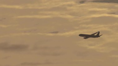 Bulutlu günbatımı gökyüzünde uçan bir jet uçağı. Seyahat, havacılık, özgürlük ve macera konuları için mükemmel.