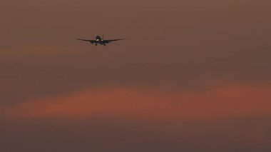 Jet uçaklarının silueti canlı bir günbatımı gökyüzüne doğru iniyor, şehirlerarası görüş..