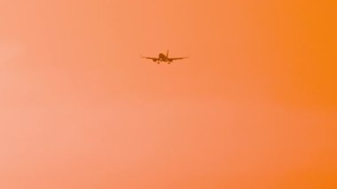 İniş için yaklaşan bir uçak, canlı altın-turuncu gün batımına karşı siluetlendi. Seyahat kavramı