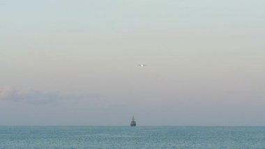 Uzakta bir kargo gemisiyle okyanusa inecek yolcu uçağı yaklaşıyor.