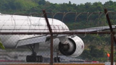 PHUKET, THAILAND - 24 Şubat 2025: Katar Havayolları Boeing 777, Phuket Havalimanı kalkış için A7-BOG ivmesi, havaalanı çitlerinden görüş