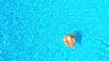 Top down view of a woman in yellow swimsuit lying on a donut in the pool. Concept of summer lifestyle, rest and relaxation