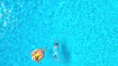 Top down view of a couple having fun in the pool, the man dives and the woman lies on an inflatable donut
