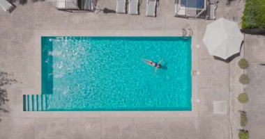 Top down view of a woman in a blue swimsuit lying on her back in the pool. Relaxing concept, summer lifestyle