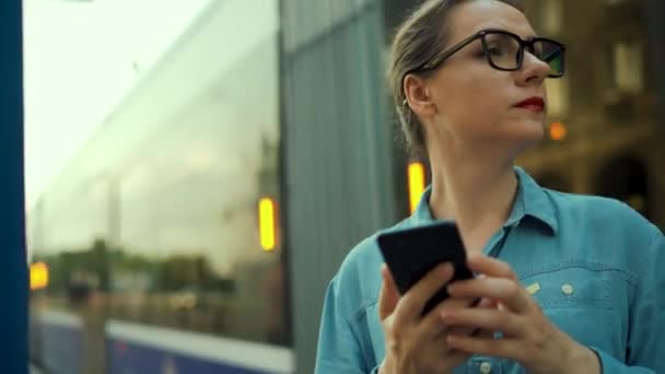 Жінка Стоїть Зупинці Громадського Транспорту Використовує Смартфон Трамвай Піднімається Тлі — стокове відео