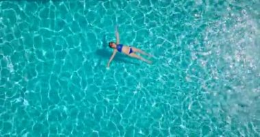 Top down view of a woman in a blue swimsuit lying on her back in the pool. Relaxing concept, summer lifestyle