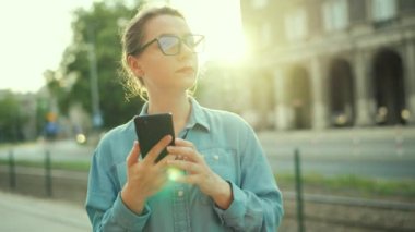 Woman using smartphone while standing outdoors at sunset. Communication, work day, busy life concept.