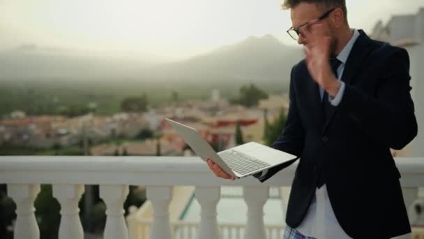在热带国家的一座别墅的阳台上 一个戴着眼镜 身穿夹克和内裤的情绪化的高加索人在家里用笔记本电脑进行谈判 离家的远程工作 — 图库视频影像