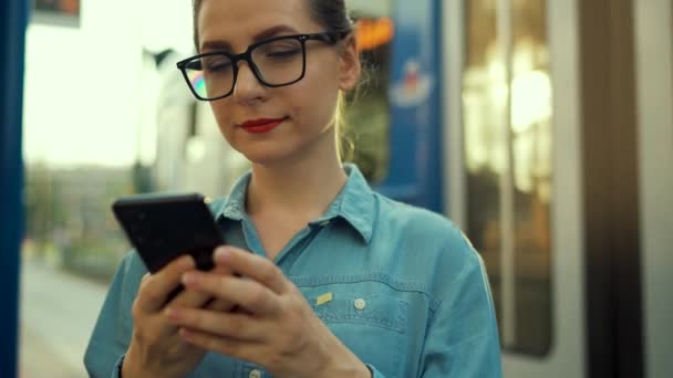 妇女站在公共交通站 使用智能手机 有轨电车停在后面 慢动作 — 图库视频影像