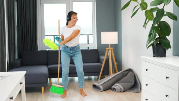 Mujer Caucásica Auriculares Limpiando Casa Divirtiéndose Bailando Con Una Escoba — Vídeo de stock