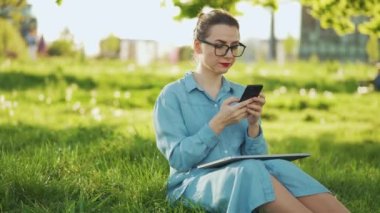 Gün batımında açık havada işi bittikten sonra parkta otururken akıllı telefon kullanan bir kadın. Dışarıda çalışan serbest çalışan biri.