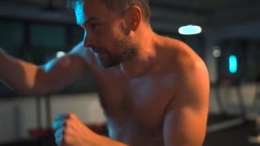 Alone male boxer is working out blows on a punching bag in a gym in evening. Slow motion