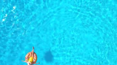 Top down view of a woman in yellow swimsuit lying on a donut in the pool. Concept of summer lifestyle, rest and relaxation