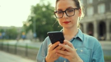Woman using smartphone while standing outdoors at sunset. Communication, work day, busy life concept.