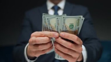 Resmi olarak giyinmiş bir adam Amerikan dolarlarını sayıyor, yakın plan. Yatırım, başarı, finansal beklentiler veya kariyer ilerlemesi kavramı.