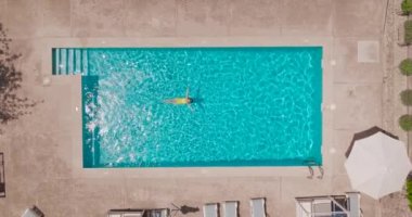 Top down view of a woman in an yellow swimsuit lying on her back in the pool. Relaxing concept, summer lifestyle