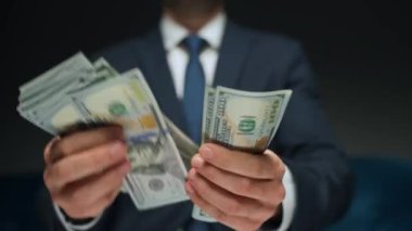 Resmi olarak giyinmiş bir adam Amerikan dolarlarını sayıyor, yakın plan. Yatırım, başarı, finansal beklentiler veya kariyer ilerlemesi kavramı.