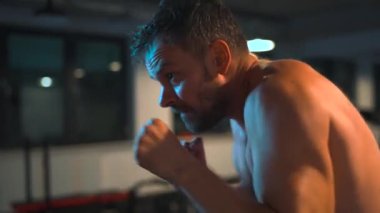 Alone male boxer is working out blows on a punching bag in a gym in evening. Slow motion