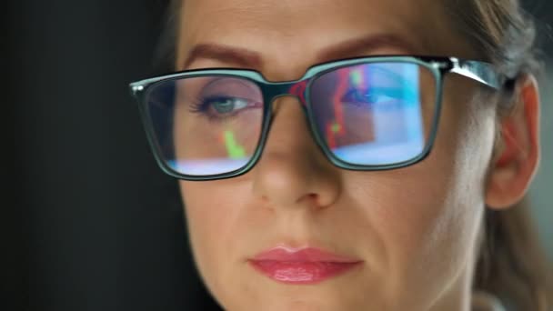 戴眼镜的女人看着监视器 用图表和分析仪器工作 显示器屏幕反映在眼镜上 晚上工作 极端密切的情况 — 图库视频影像