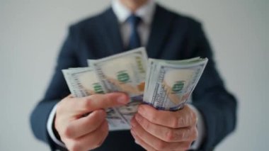 Resmi olarak giyinmiş bir adam Amerikan dolarlarını sayıyor, yakın plan. Ağır çekim. Yatırım, başarı, finansal beklentiler veya kariyer ilerlemesi kavramı.