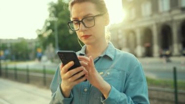 Gün batımında dışarıda dikilirken akıllı telefon kullanan bir kadın. İletişim, iş günü, yoğun yaşam konsepti. Yavaş çekim