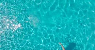 Sarı mayo giymiş bir kadının havuzda sırt üstü yatışı. Rahatlatıcı konsept, yaz yaşam tarzı. Kamera suyun üzerinde yükseliyor.