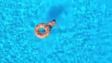 Havuzda şişme donutla yüzen kırmızı şortlu bir adamın hava görüntüsü. Yaz yaşam tarzı