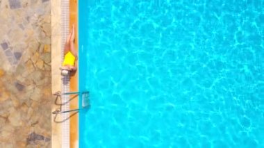 Sarı mayolu ve şapkalı bir kadın havuzun kenarında oturuyordu. Yaz yaşam tarzı, dinlenme ve rahatlama kavramı